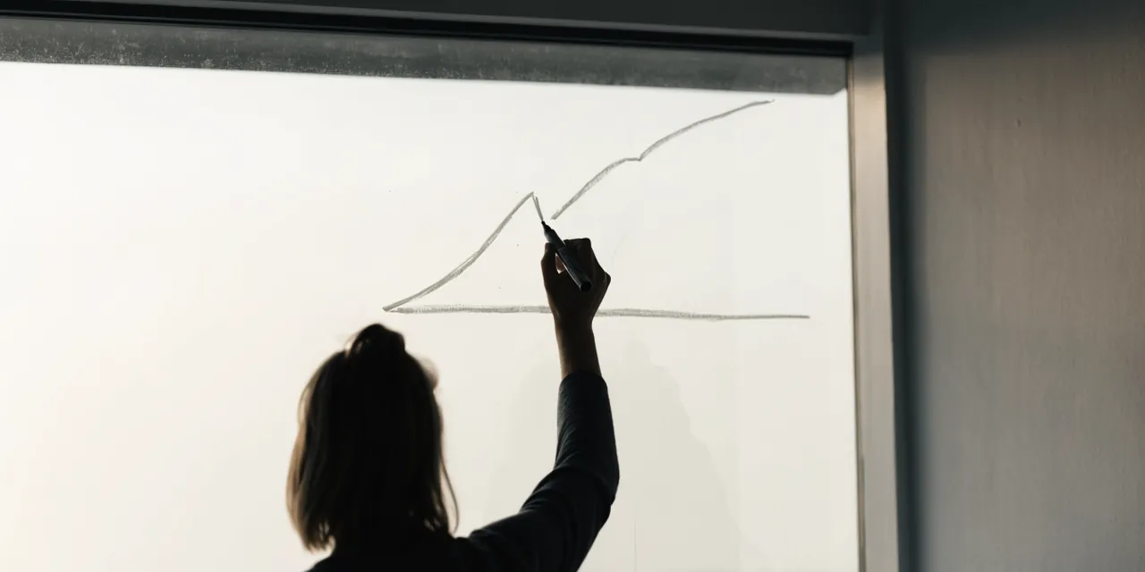 A person at a glass wall marking a rising line above a straight baseline.