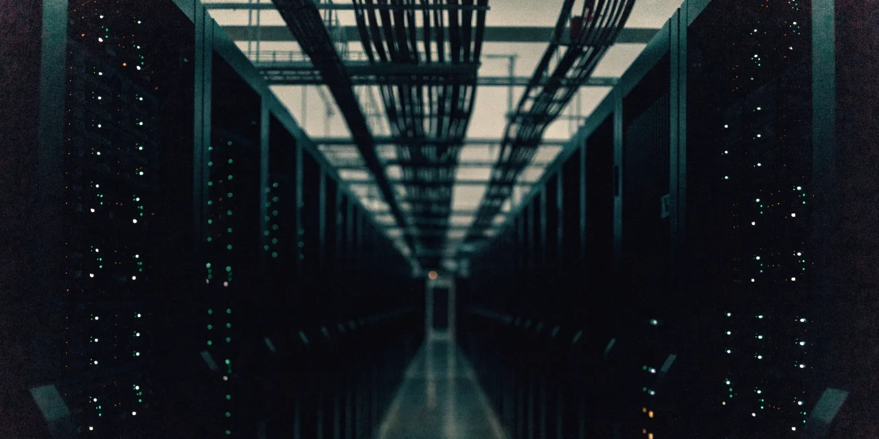 A server room aisle lit by indicator lights, cabling running overhead.