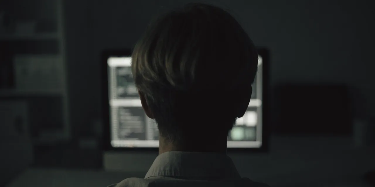 A person working alone at a monitor in a dim office at night.